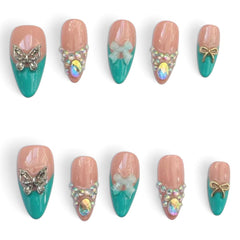 Press-on Nail | Y2K Turquoise French V-Tip Style | Almond Shape- Ten false press-on nails arranged in two rows on a plain white background. The nails have a glossy peach-pink top half and a teal-green bottom half, decorated with butterfly, bow, rhinestone, and iridescent oval embellishments in silver, white, and gold tones.