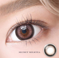 Close-up of an eye wearing brown contact lenses with 'Secret Milktea' label.