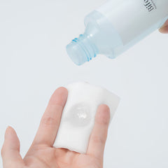 A hand holds a white cotton pad while a hand holds a frosted bottle above it, pouring a clear gel onto the pad. The bottle has the brand name 'BiFe' printed on it.-Bifesta Eye & Lip Makeup Remover 145ml-THE COSMETIC STORE NZ