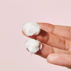 COSRX Balancium Comfort Ceramide Cream 80g- White earbud cases held between fingers against a pink background