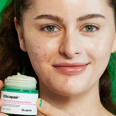 Woman holding a jar of Cicapair Dr. Jart+ product with a close-up of her face.