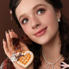Woman holding a heart-shaped cookie charm with a bow - Flower Knows Sweetie Bear Mini Setting Powder 01 Cocoa for smooth and long-lasting makeup