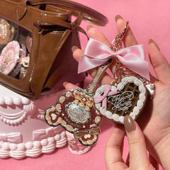 Decorative keychain with pink bow held by a hand, with a brown handbag in the background.- Flower Knows Sweetie Bear Mini Setting Powder 01 Cocoa luxury bear-themed packaging