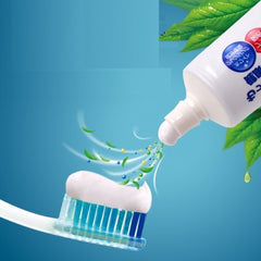 A close-up commercial shot of toothpaste being squeezed from a white tube onto a toothbrush with blue and white bristles. Green leaf graphics and floating green droplets suggest mint flavor or freshness, set against a blue gradient background.-Lion White & White Toothpaste 150g [Domestic Version]-THE COSMETIC STORE NZ.