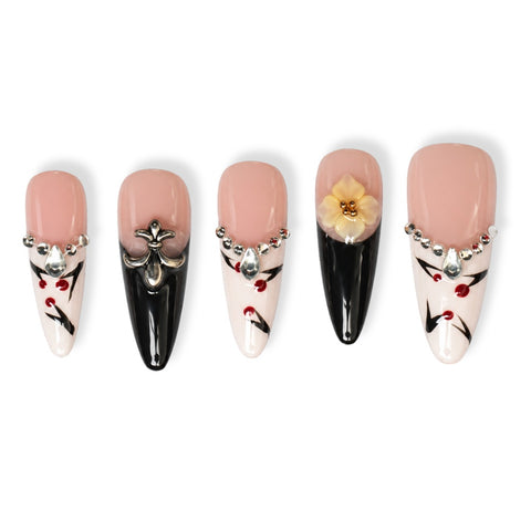Five coffin-shaped press-on nails with a pale pink base, decorated with black, white, red, silver, and yellow nail art details, displayed on a clean white background.