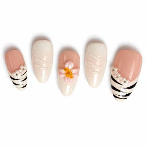 Five almond-shaped press-on nails displayed on a white background. The set features a nude pink base with black and white zebra stripes on the ends of two nails, one nail with a pink and white flower design with a yellow center, and two plain cream-colored nails.