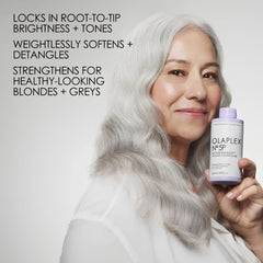 Woman with gray hair holding a bottle of Olaplex, with product features listed on the left.