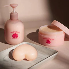 A pink pump bottle of body lotion, a pink jar of body soap scrub with its lid off, and a heart-shaped soap bar on a marble tray, all in a warm, softly lit setting.- Pelican Soap Attractive Hip Care Soap 80g | Butt Whitening & Scrub- The Cosmetic Store New Zealand