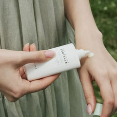 Person applying Centella cream to their wrist with a blurred green background