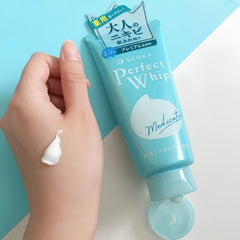Senka Perfect Whip Acne Care Face Wash 120g | Acne Cleanser NZ-Hand applying cream from a blue Senka Perfect Whip tube against a light blue background