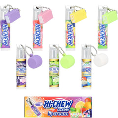 Six mini Hi-Chew lip balm tubes with attached colorful rectangular keychains and silver keyrings, shown above a retail box of Hi-Chew Lipcarem. The lip balms come in purple, pink, yellow, green, orange, and white flavors, and the box features fruit illustrations including citrus, berries, and strawberries.
