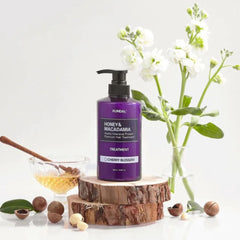 Kundal Honey & Macadamia hair treatment bottle on a wooden block with flowers and honeycomb in the background.