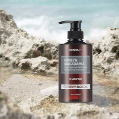 Kundal Honey & Macadamia shampoo bottle on a rocky beach