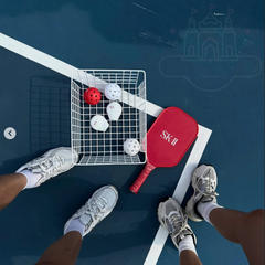 Top-down view of a pickleball game with balls and paddles on a blue court.-SK-II Genoptics CC Primer bottle -tone up primer- available at The Cosmetic Store New Zealand