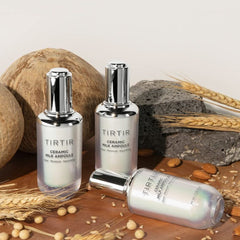 Three TIRTIR ceramic milk ampoules on a wooden surface with natural elements.