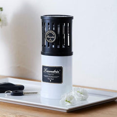 White and black cylindrical product with 'Laundrin' branding on a tray with flowers and keys.