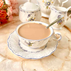 Cup of tea with a spoon on a saucer, set against a floral background