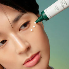 Person applying a green eye cream to their face with a blurred background