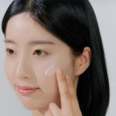 Woman applying cream to her face with a neutral background