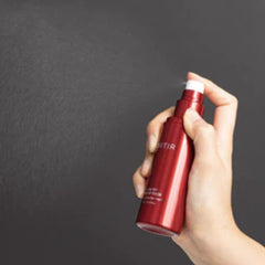 Hand holding a red spray bottle with a dark background