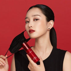 Woman holding a red cosmetic bottle against a red background