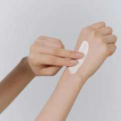 Person applying a white cream or lotion to their arm against a light gray background