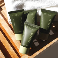 Four Wildhife body care tubes arranged on a wooden tray with a white towel in the background. The tubes are olive green with pale yellow caps and gold lettering, showing products including body wash, body lotion, shampoo, and conditioner.-Wildheke Essential Travel Kit 4x25ml mini bottles with pouch at The Cosmetic Store NZ.