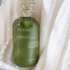 A bottle of Wildheke Laundry Liquid in a translucent olive green bottle with a beige pump dispenser, nestled inside white textured fabric.Sleek Wildheke eco friendly plant based laundry detergent 500ml sitting on a modern laundry shelf NZ.
