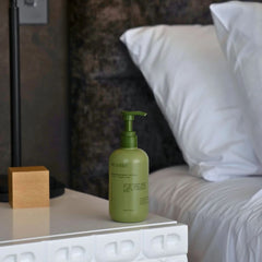 A green pump bottle of Green Roots Turmeric Curcumin capsules sits on a white bedside table next to a bed with white pillows in a modern bedroom setting.- Wildheke therapeutic magnesium body lotion 300ml sitting on a modern bedside table NZ.-THE COSMETIC STORE NZ.