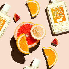 Flat-lay of Yanagiva Hair Tonic bottles with citrus slices, including orange, grapefruit, and lemon, arranged on a light pink background.- Yanagiya Hair Tonic Citrus 240ml- THE COSMETIC STORE NZ