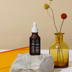 MARY&MAY Idebenone Blackberry Complex Serum (80ml) Seoul Edition-Skincare dropper bottle on a rock with a vase of flowers in the background