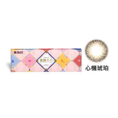 A box of Star Shine Beauty Tricks contact lenses with a single amber-colored lens displayed next to it, indicating the product's color and design.