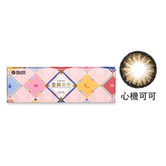 A box of Star Shine Beauty Tricks Coco Brown color contact lenses with a few lenses displayed outside the box. The packaging is predominantly pink with multi-colored lenses visible and a logo at the top.